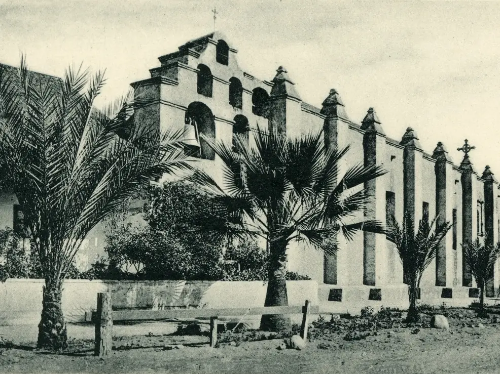 Hand-colored 1903 postcard of the San Gabriel Mission with palms in front of its buttressed wall